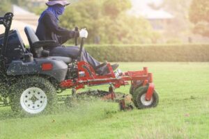 A solo entrepreneur loads a commercial lawn mower onto a trailer at dawn, ready for a day of yard maintenance services